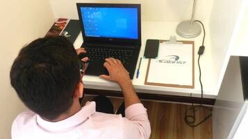 Una persona sentada en un escritorio, con una computadora portátil, un teléfono inteligente y un portapapeles con un nombre.