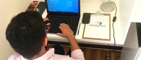 Una persona sentada en un escritorio, con una computadora portátil, un teléfono inteligente y un portapapeles con un nombre.