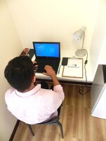 Una persona sentada en un escritorio, con una computadora portátil, un teléfono inteligente y un portapapeles con un nombre.