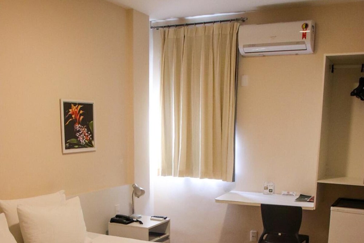 Habitación de hotel con una cama grande, un escritorio, una silla, un refrigerador pequeño y un equipo de aire acondicionado.