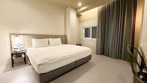 Una habitación de hotel con una cama grande, una mesita de noche con lámpara, una ventana y una cortina.
