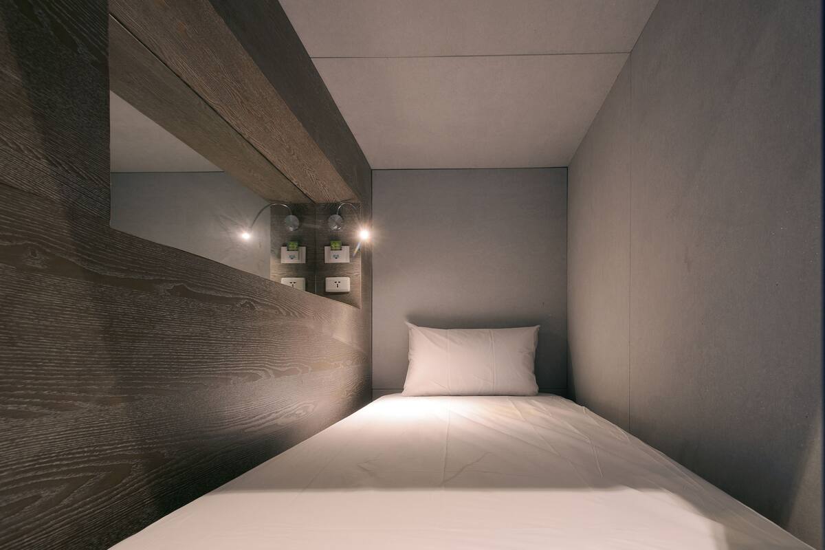 A modern bedroom with a wooden accent wall, a white bed, and a small bedside table with a lamp.