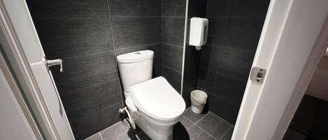 Un baño pequeño y moderno con inodoro, secamanos y cubo de basura.