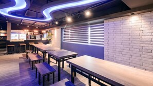 Un interior de restaurante moderno con mesas y bancos de madera, una pared de ladrillo y una ventana con persianas.