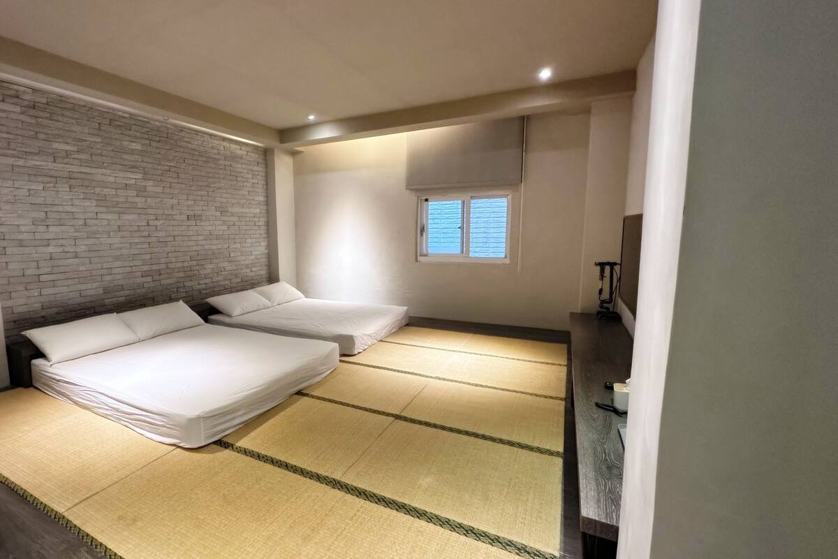 A room with two beds, a brick wall, a small window, and a tatami mat floor.