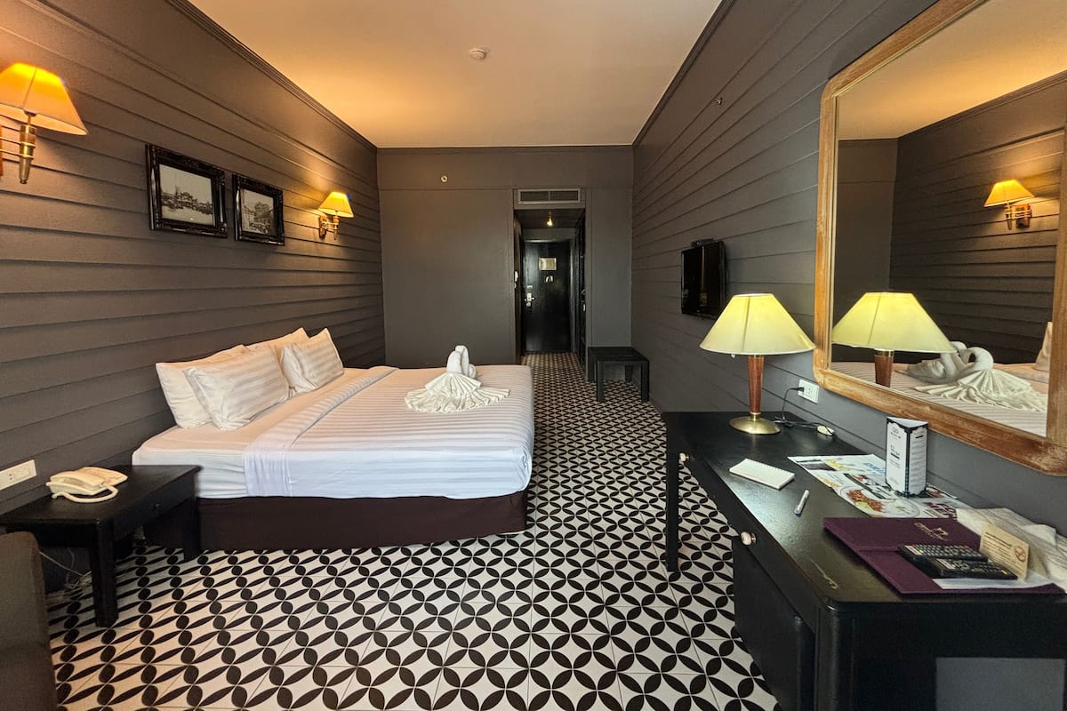 Habitación de hotel con cama, mesita de noche, lámpara y un espejo grande.