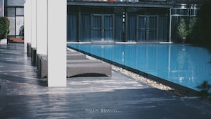A poolside area with wicker lounge chairs and a clear blue pool. - Napalai Hotel (Udon Thani)