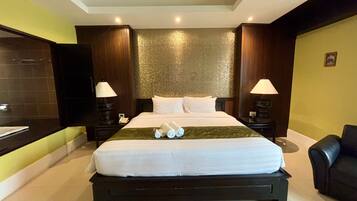Habitación de hotel con una cama grande, dos mesitas de noche con lámparas, un cabecero de madera, un televisor montado en la pared y un baño con un espejo grande y un perchero para toallas.
