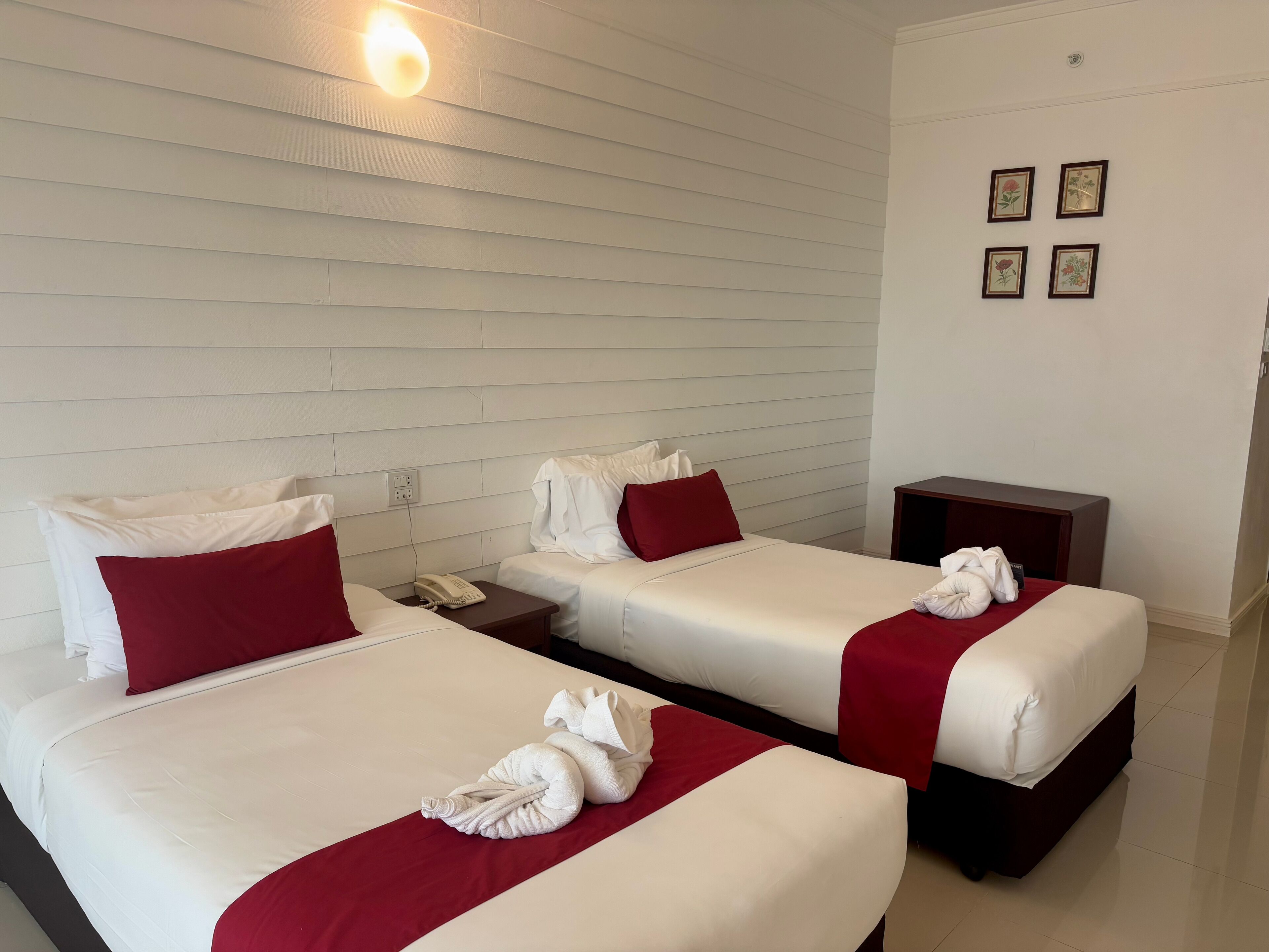 Ein Hotelzimmer mit zwei Betten, jeweils mit weißer Bettwäsche und roten Kissen, einem Nachttisch mit Telefon und einer Wandleuchte.