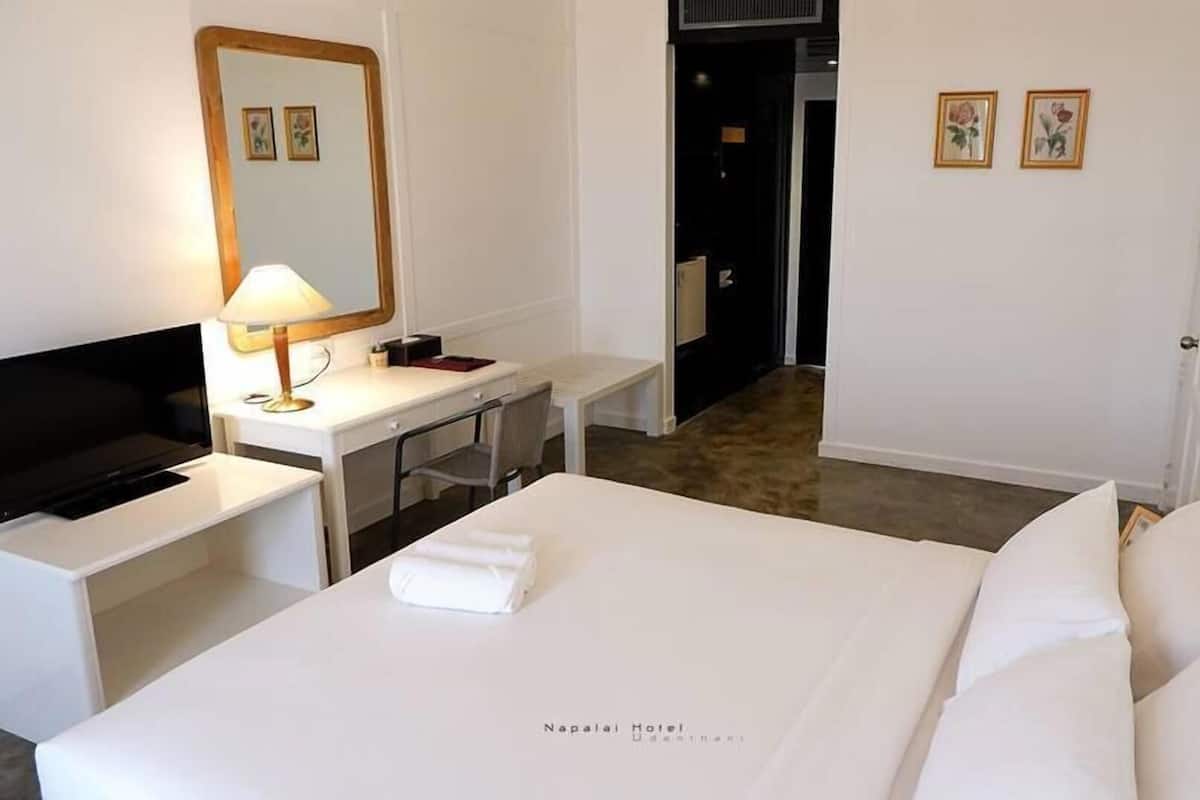 Una habitación de hotel con cama, escritorio con televisor, espejo y dos cuadros en la pared.