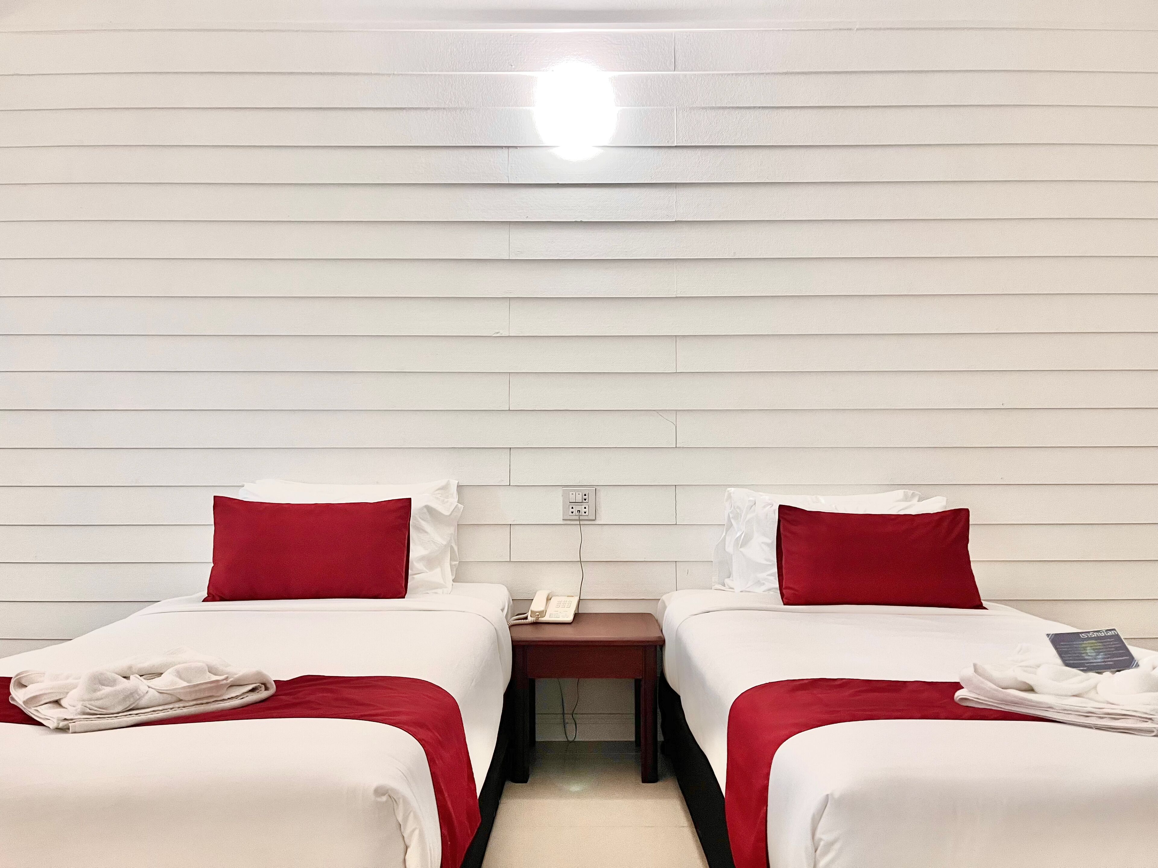 Ein Hotelzimmer mit zwei Betten, jeweils mit roter und weißer Bettwäsche, einem kleinen Nachttisch mit Telefon und einer wandmontierten Lampe.