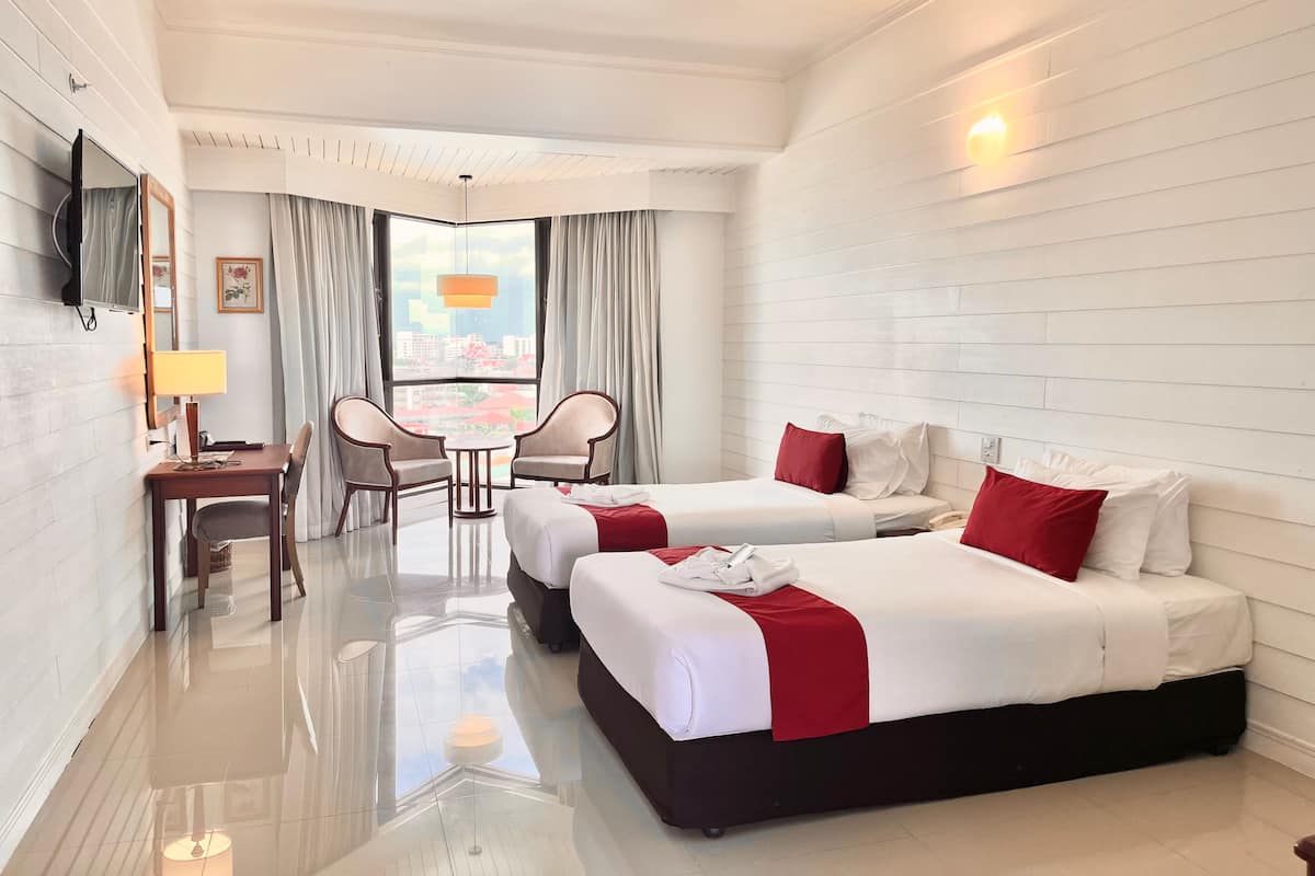 Habitación de hotel con dos camas, un escritorio con silla, televisión y un ventanal con cortinas.