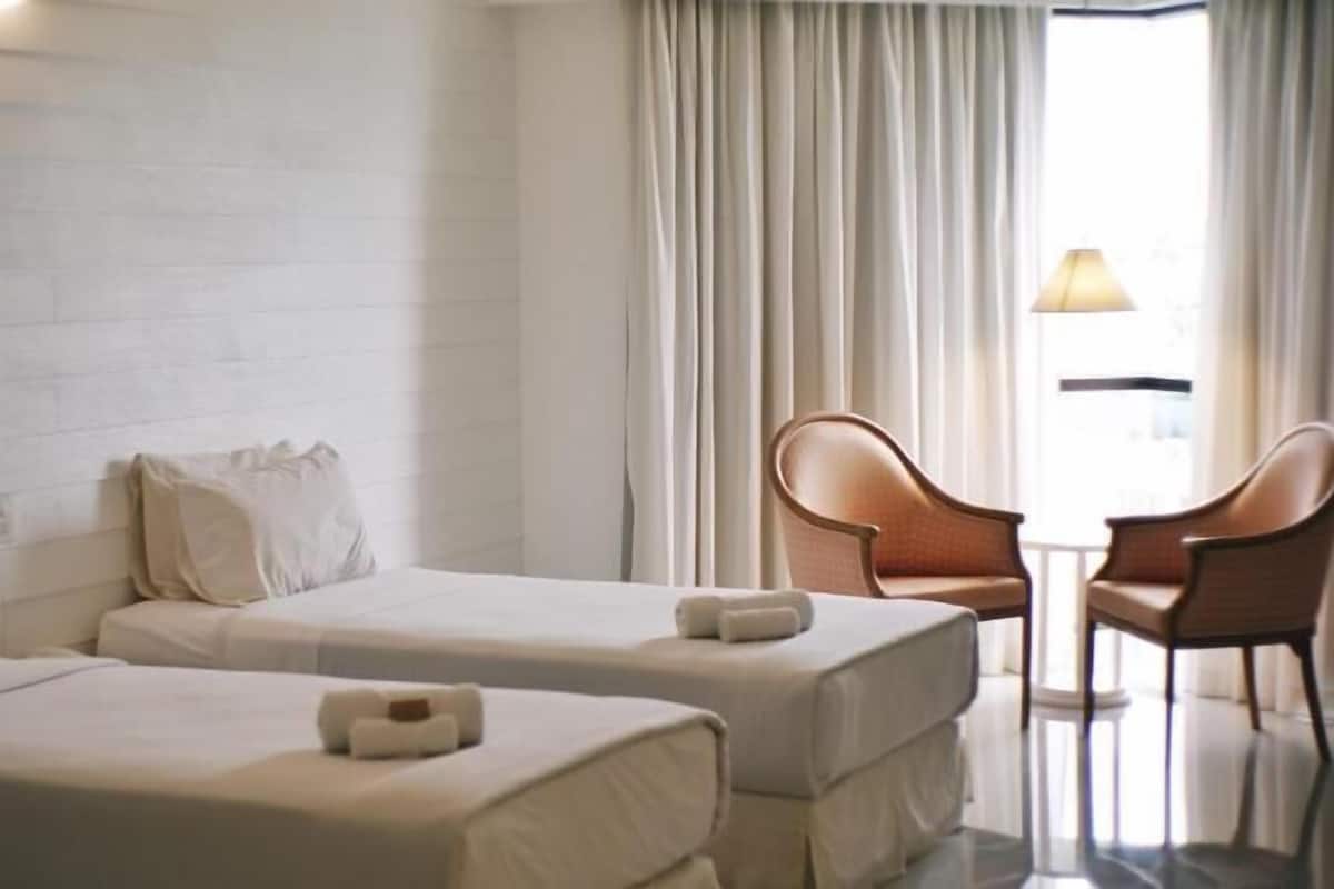 Una habitación de hotel con dos camas, una mesita, dos sillas y una ventana con cortinas.