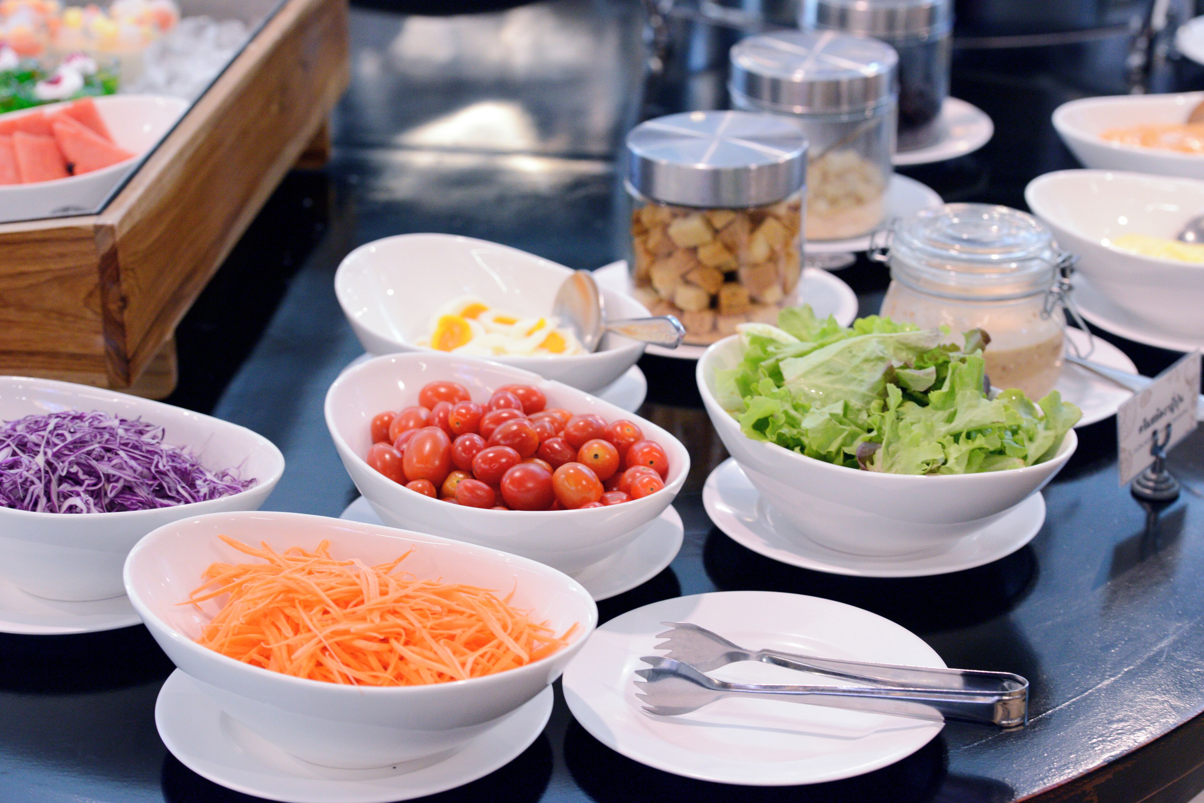 A buffet table with various food items including salads, shredded vegetables, and a bowl of cherry tomatoes.