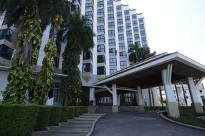 Un edificio moderno con un acceso cubierto, escalones que lo conducen y follaje circundante.