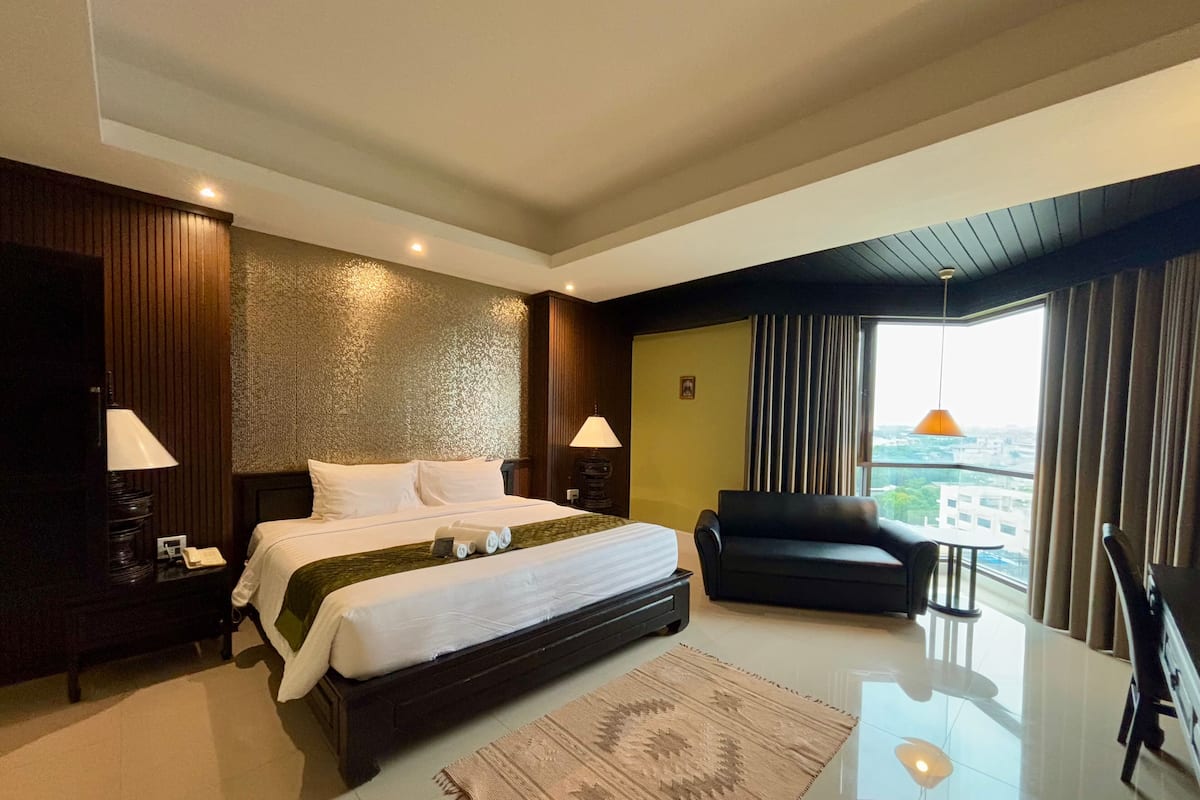 Habitación de hotel moderna con una cama grande, un sofá, vistas a la ciudad y un balcón.