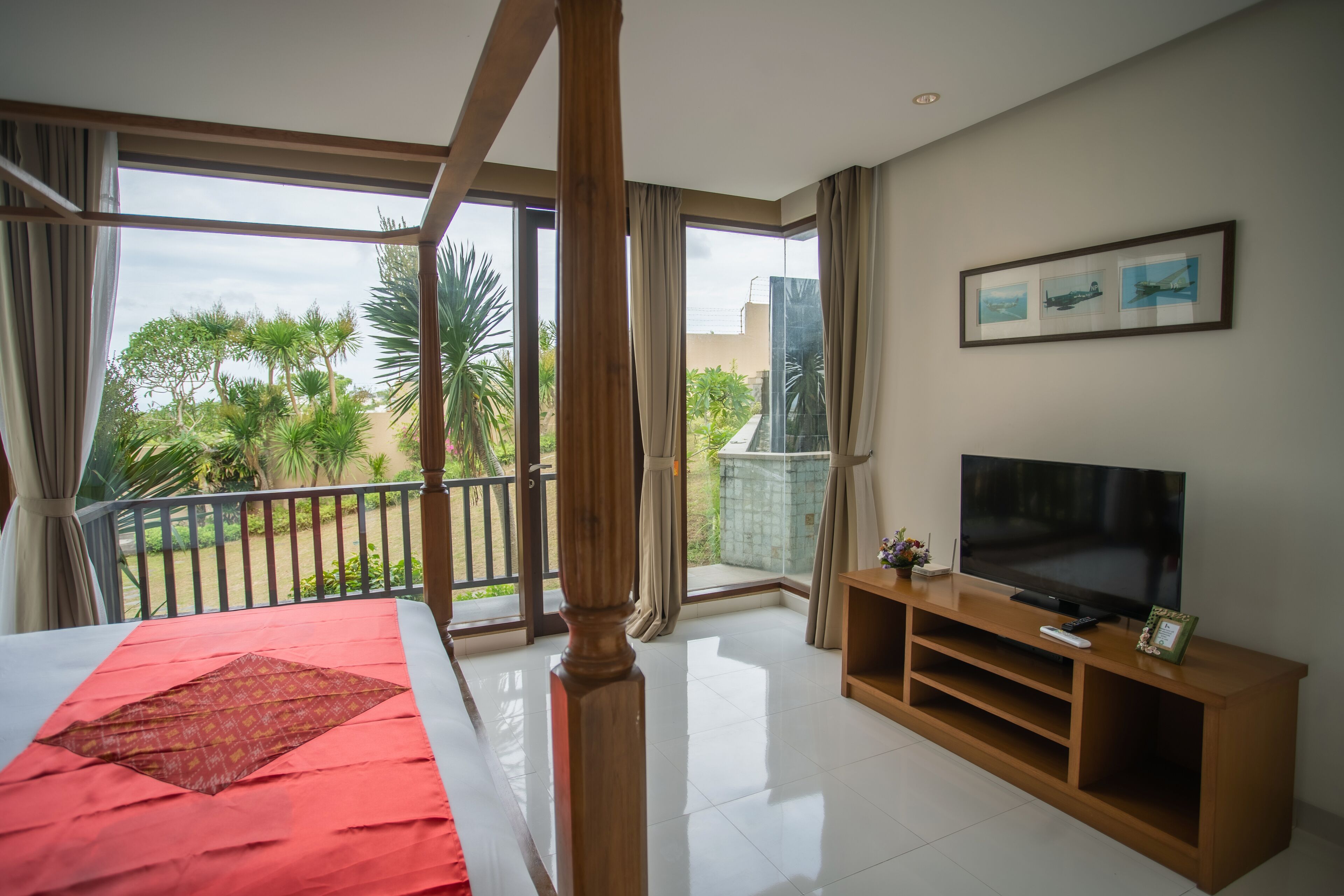 A bedroom with a large bed, a TV on a wooden stand, and a balcony with a view of greenery.
