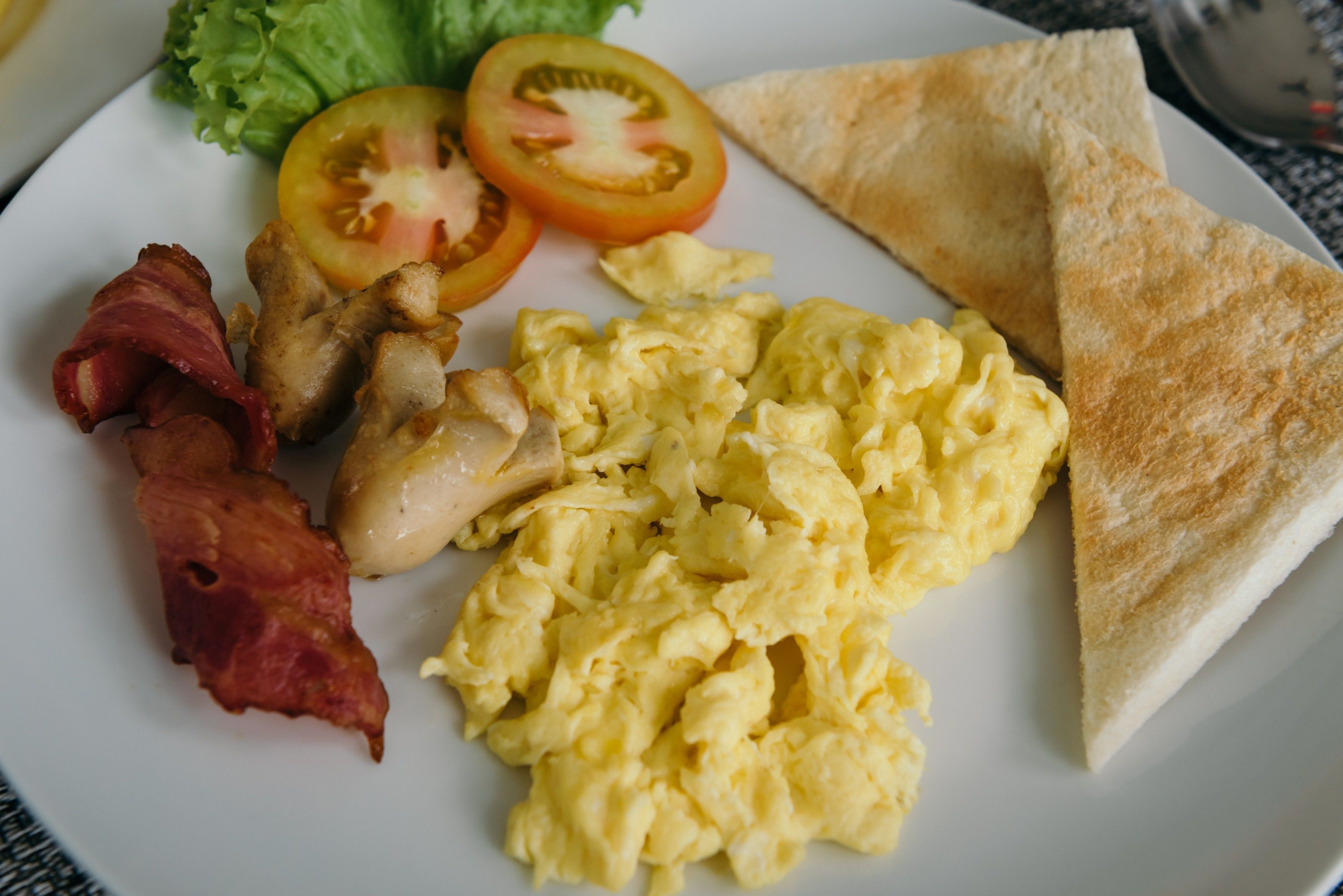 A plate with scrambled eggs, bacon, two tomato slices, and a piece of toast.