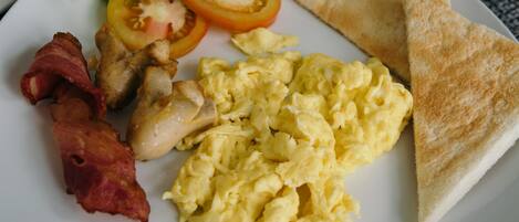A plate with scrambled eggs, bacon, two tomato slices, and a piece of toast.