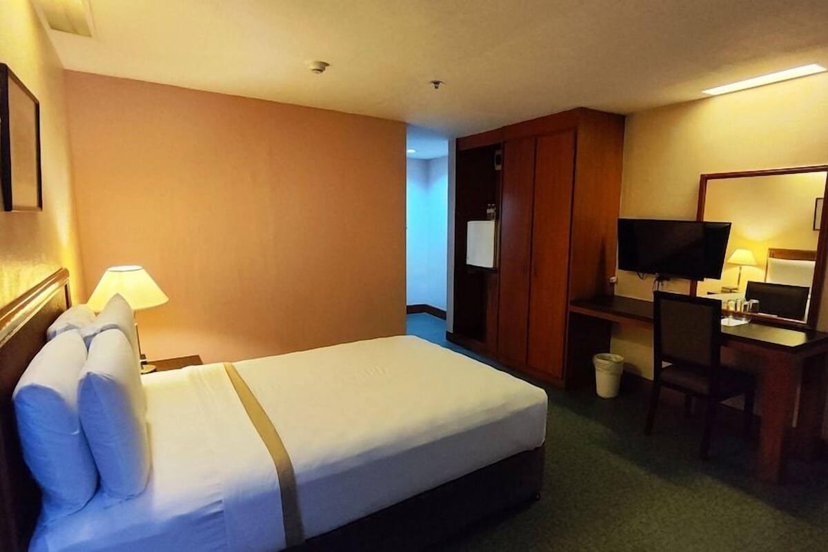 Una habitación de hotel con cama, escritorio, silla, televisor y espejo.
