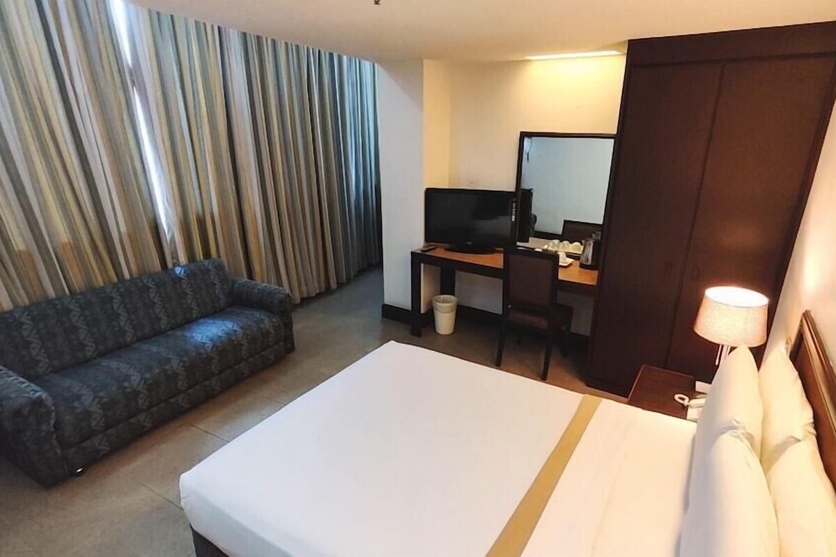 Una habitación de hotel con cama, sofá, escritorio con computadora, televisor y espejo.