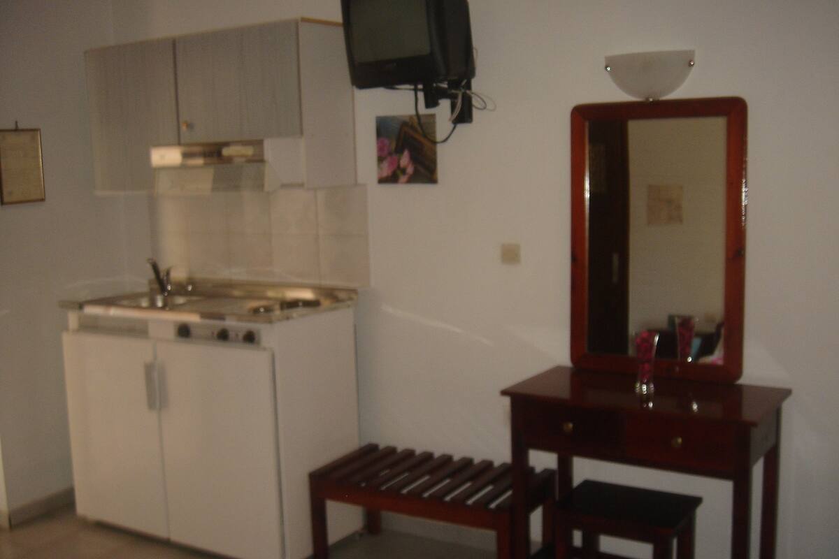 Uma cozinha compacta com fogão, pia e um pequeno banco de madeira.