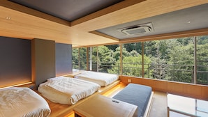 Una habitación moderna con dos camas, una mesita pequeña y grandes ventanales con vistas a un bosque.