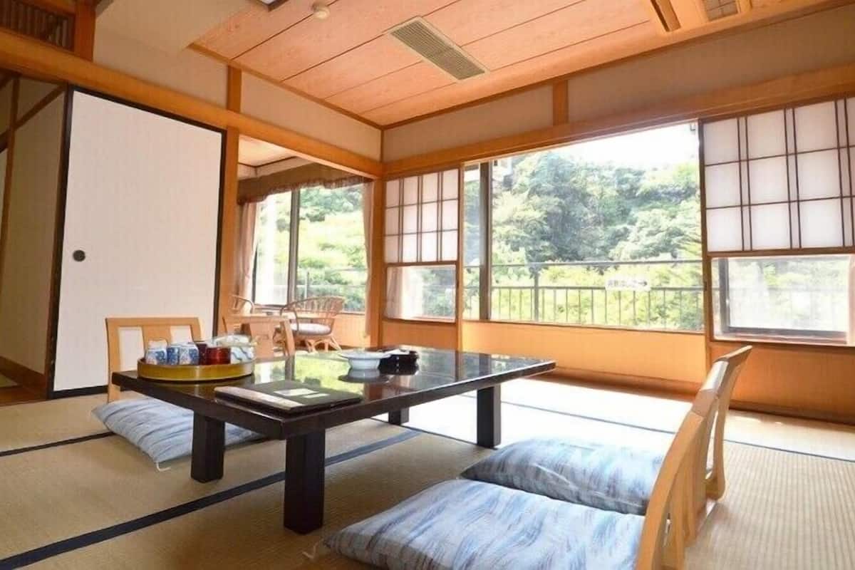 A traditional Japanese room with tatami flooring, a low table with cushions, and large windows offering a view of greenery.