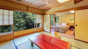 Una habitación japonesa tradicional con suelo de tatami, una mesa de madera y vistas a un bosque a través de amplios ventanales.