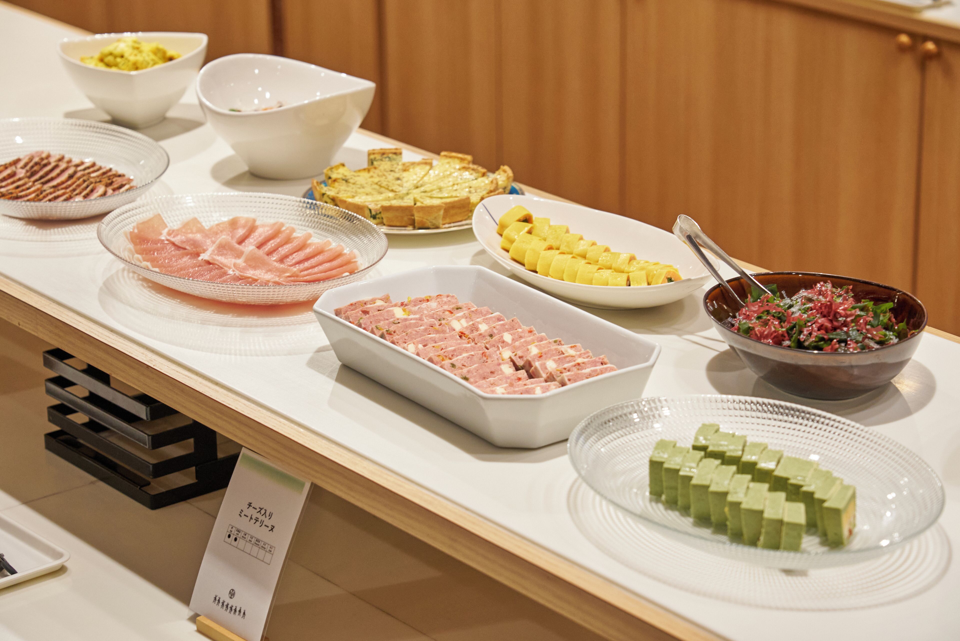 A buffet with various dishes including sliced meats, a quiche, pineapple chunks, and a salad.