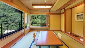 Una habitación japonesa tradicional con suelo de tatami, una mesa de madera y vistas a una zona boscosa.