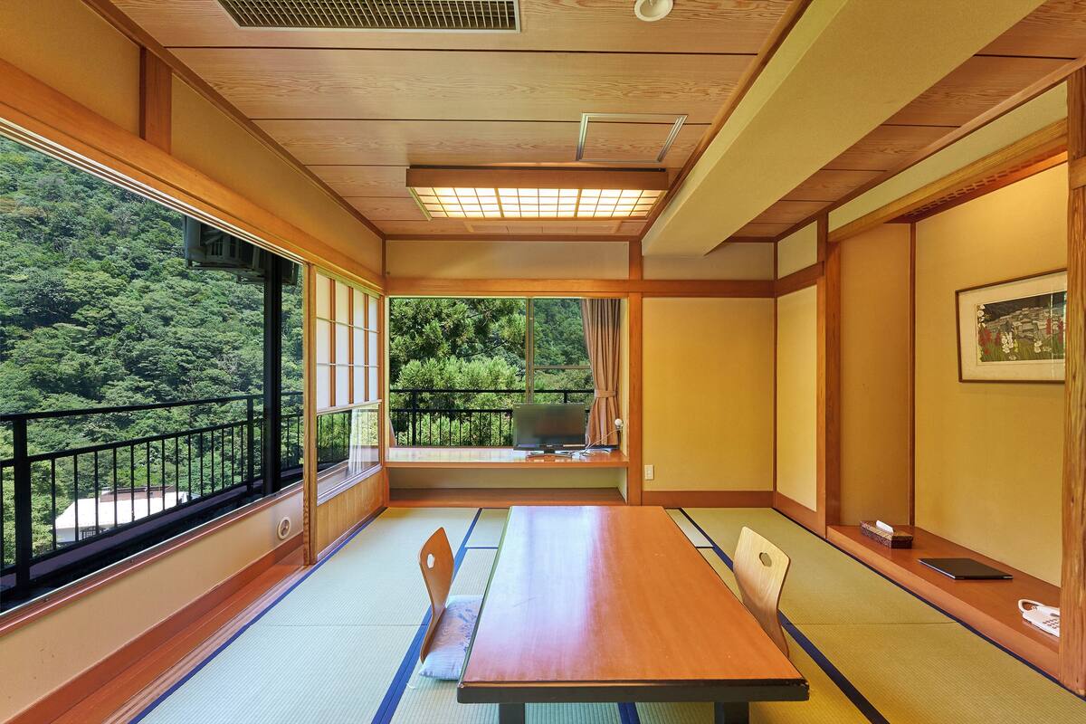 A traditional Japanese room with tatami flooring, a wooden table, and a view of a forested area.