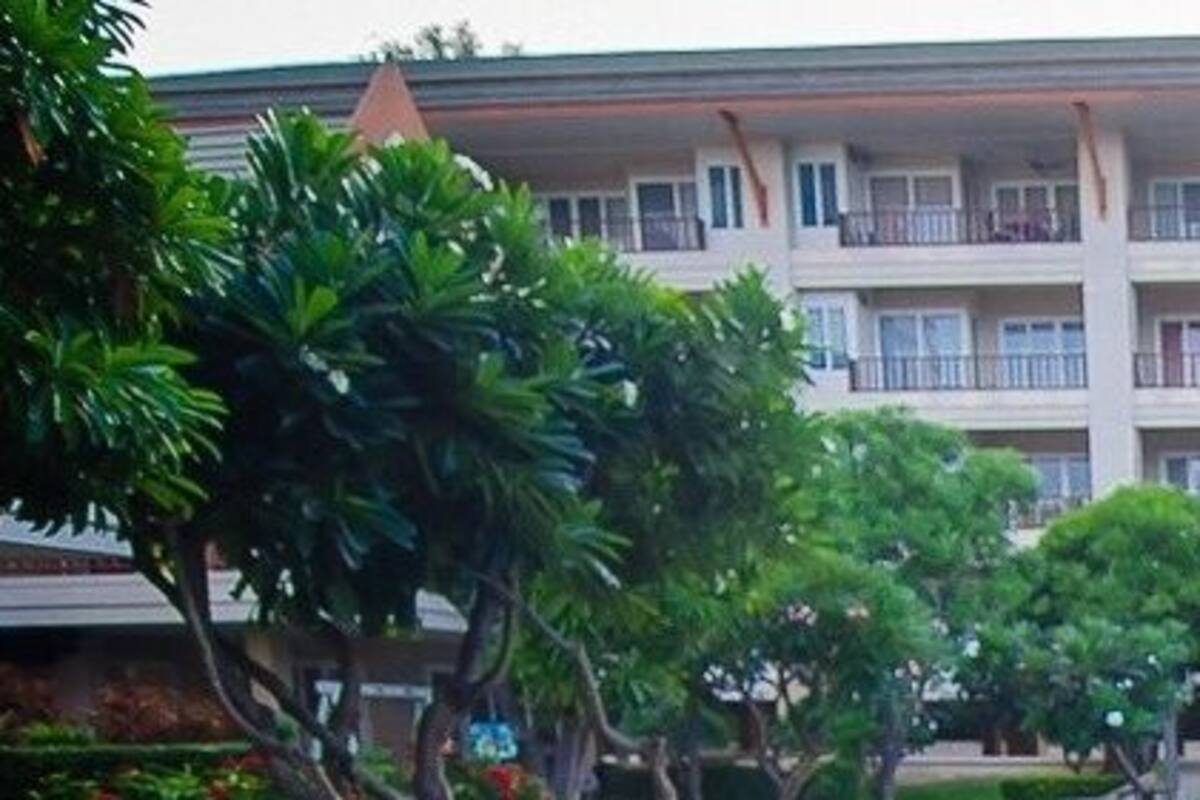 A multi-story hotel with balconies, surrounded by lush greenery.
