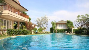A swimming pool with a tiled deck, surrounded by lush greenery and two buildings with balconies. - Talay Samran by Lease Back Thailand (Cha-am)