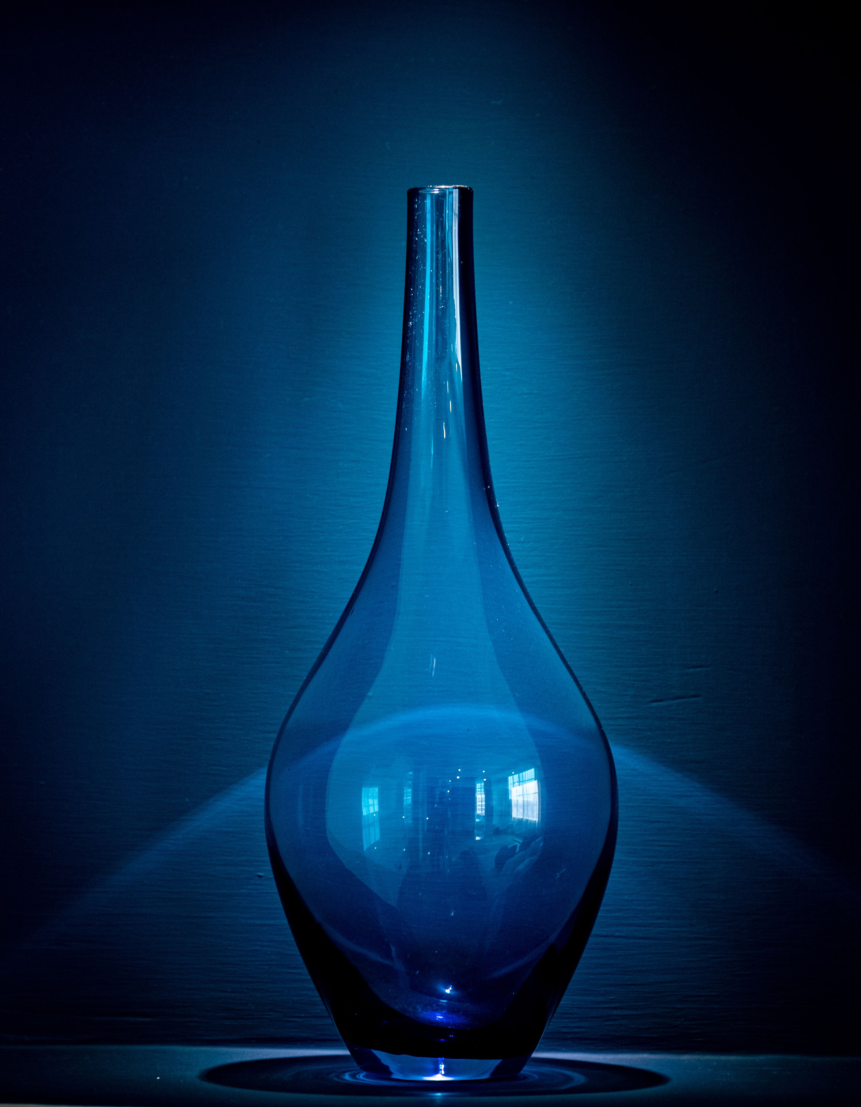 Eine transparente, schmalhalsige Vase mit breiter Basis auf einer spiegelnden Oberfläche.