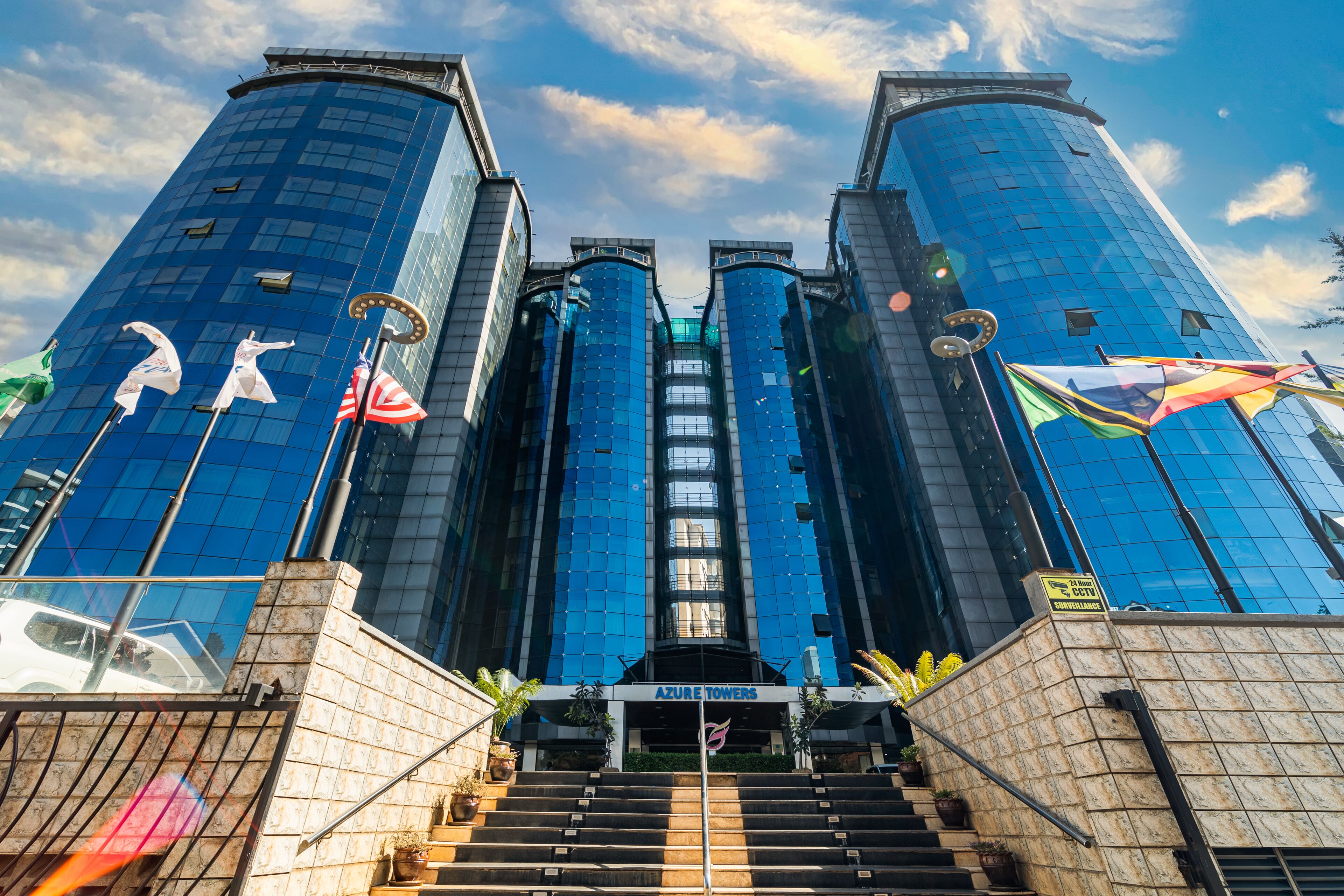 A modern building with a glass facade, a central entrance, and multiple flags.