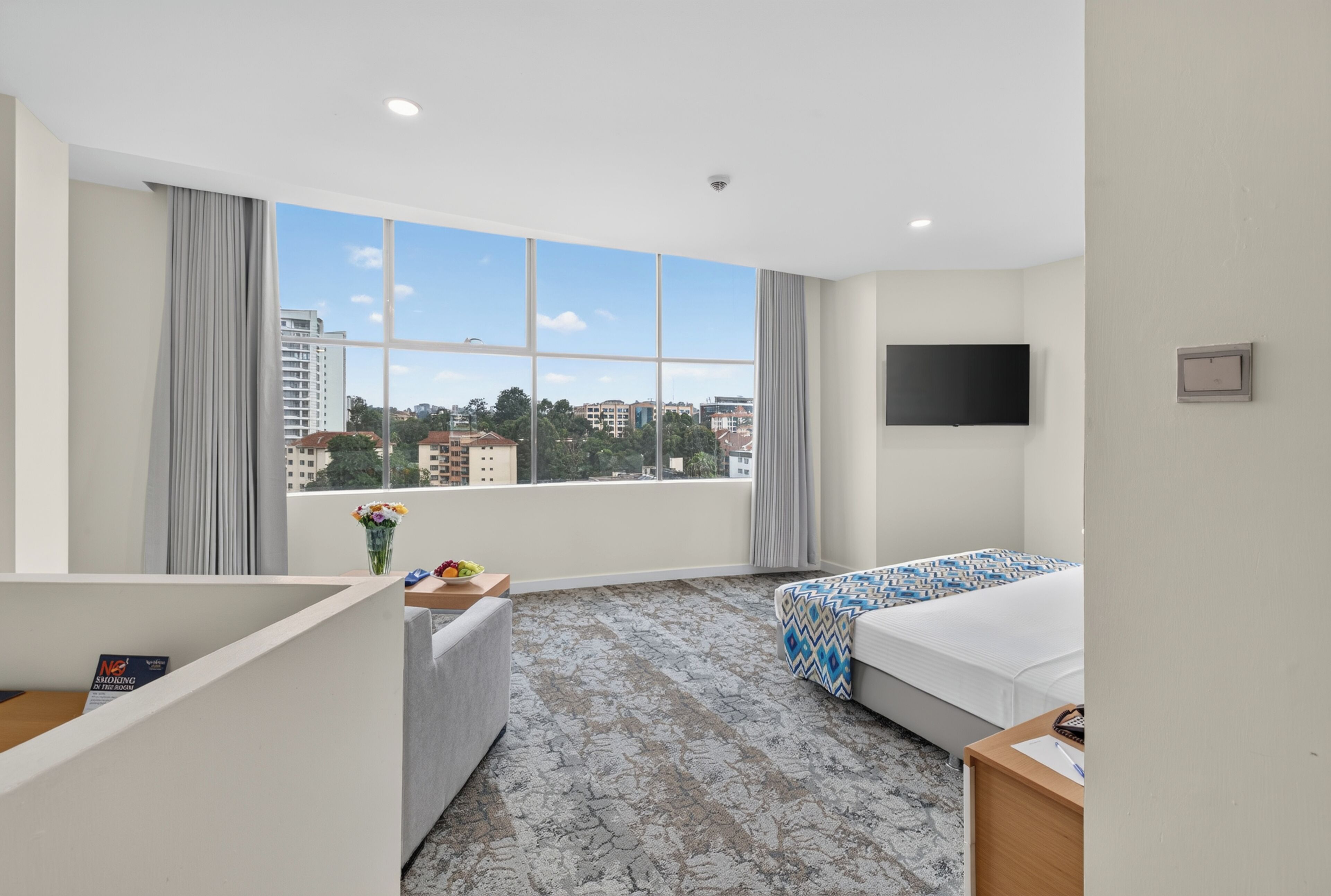 A hotel room with a large window, a bed, a desk, and a TV.