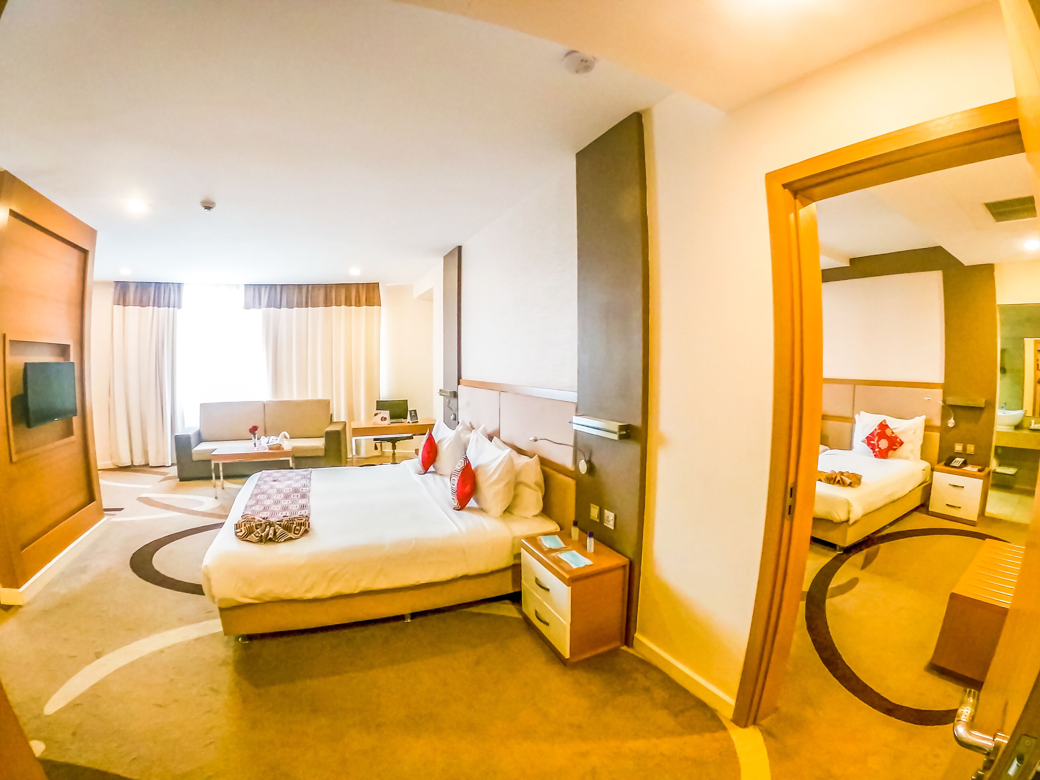 Une chambre d’hôtel comprenant un lit, des tables de chevet, un bureau, une chaise, un canapé, un grand miroir et une vue sur l’extérieur.