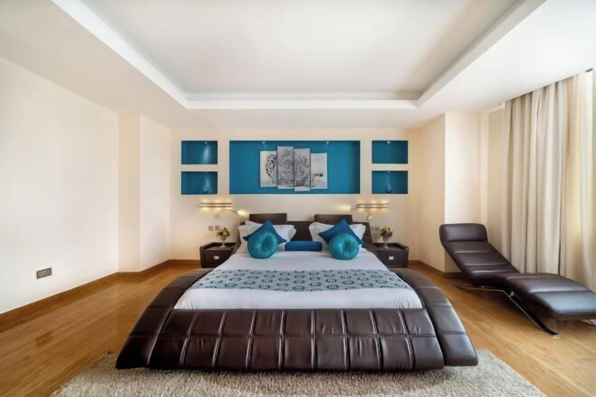 A bedroom with a large bed, bedside tables, a reclining chair, and artwork on the wall.