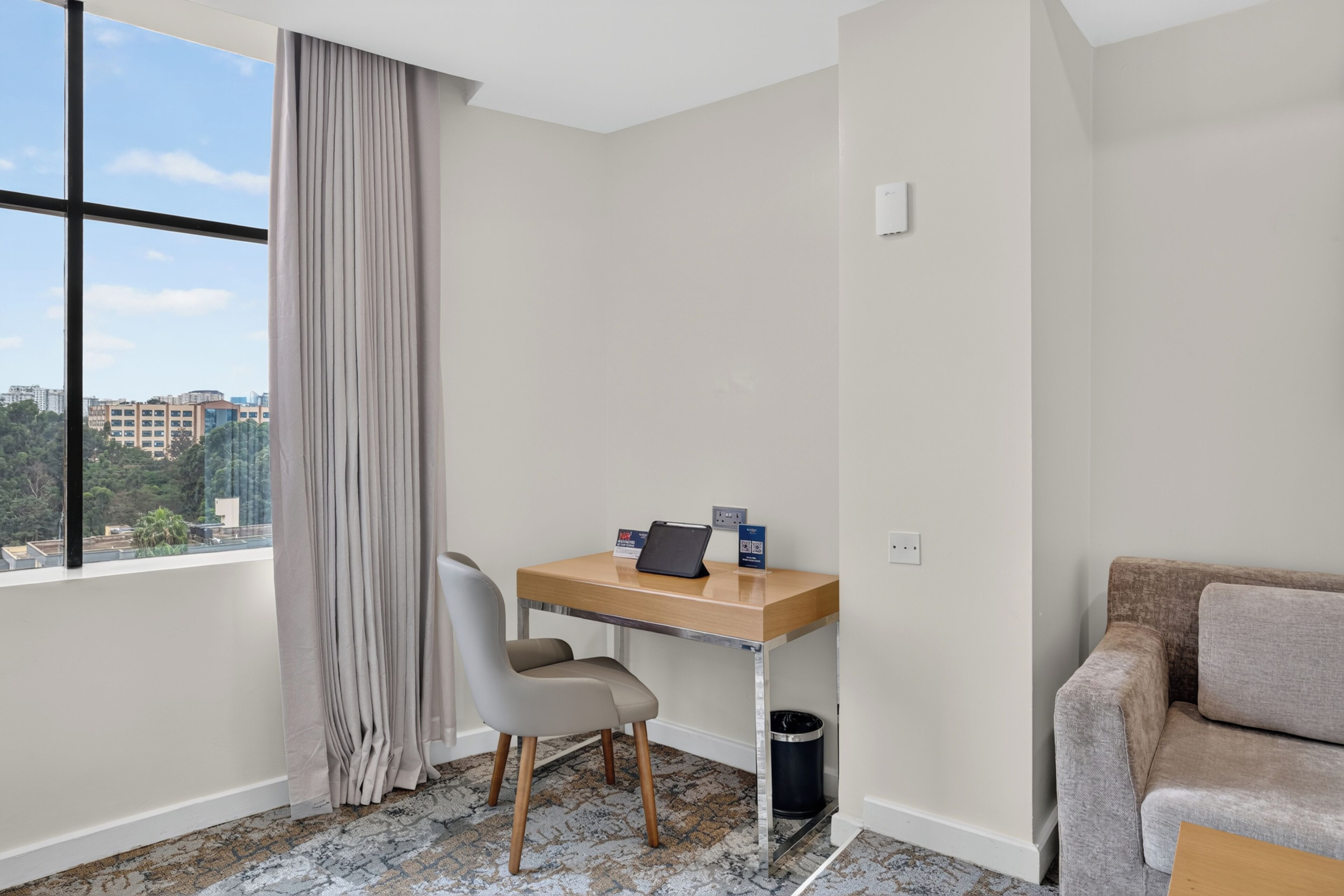 A hotel room with a desk, chair, and a sofa.