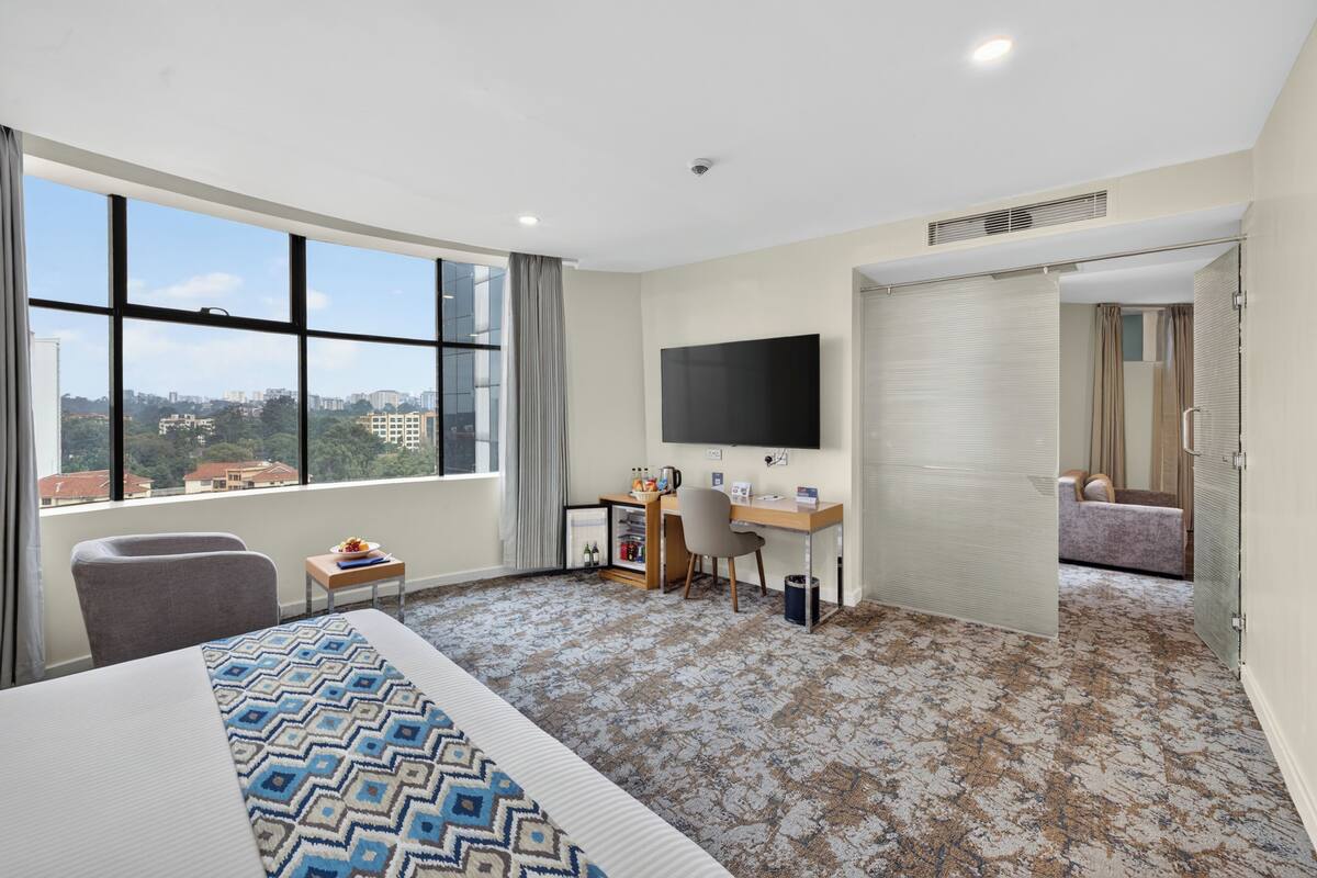 A hotel room with a bed, a desk, a TV, and a view of the city.