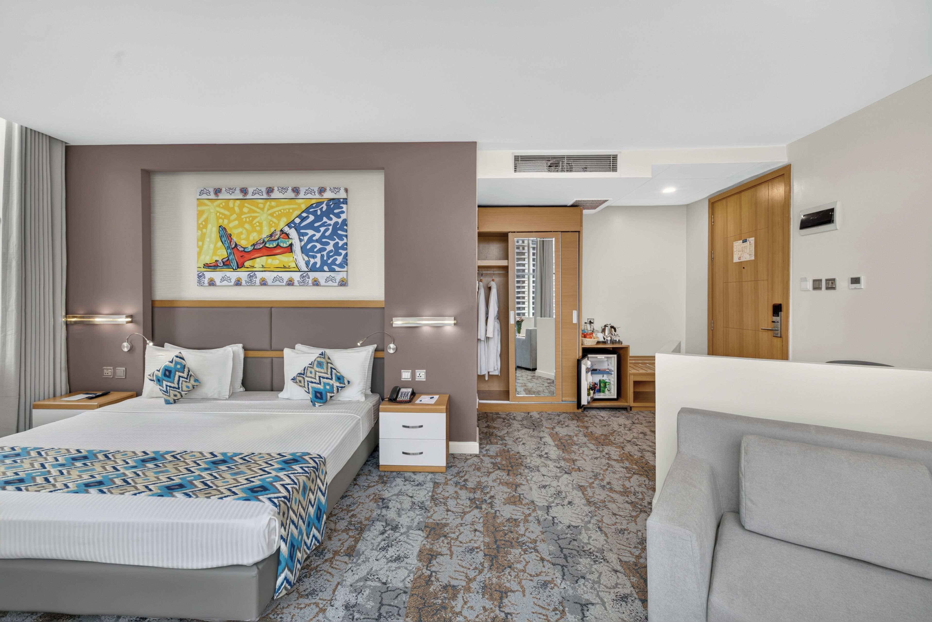 Une chambre d’hôtel comprenant un lit, des tables de chevet, un canapé, une salle de bain avec un miroir et une armoire.