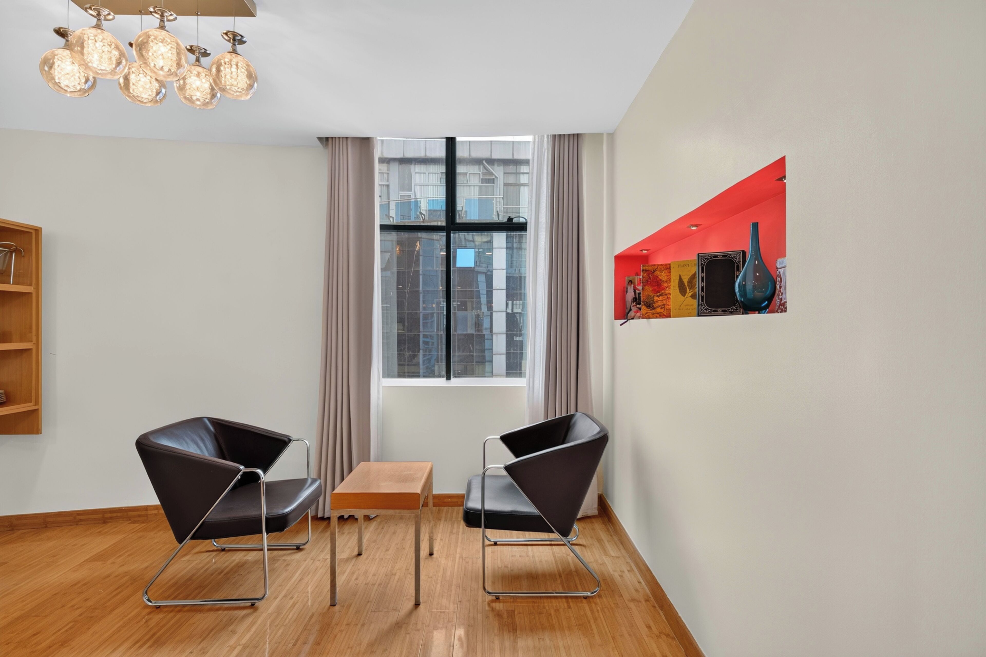 Une pièce moderne avec deux chaises noires, une petite table en bois, une grande fenêtre avec des rideaux et un luminaire suspendu.