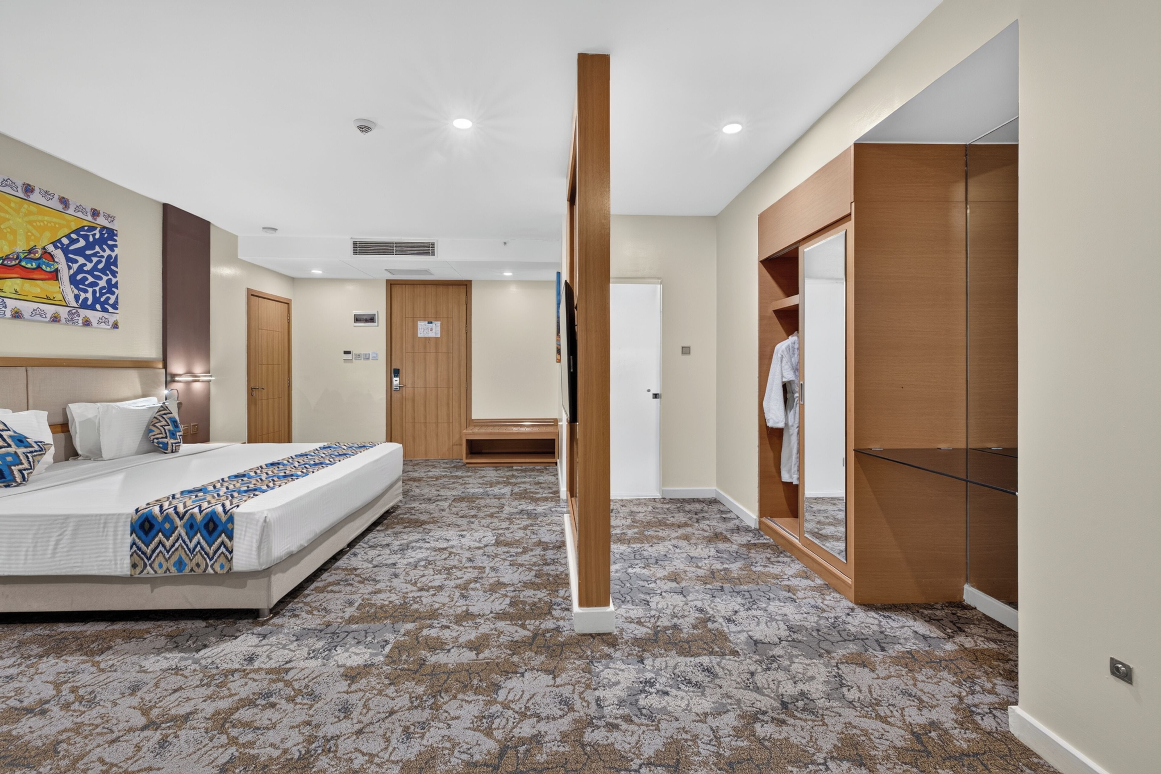 A hotel room with a bed, a wardrobe, a mirror, and a door leading to a bathroom.