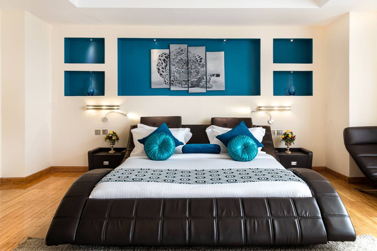 A modern bedroom with a large bed, blue accent pillows, and a leopard print artwork above the bed.