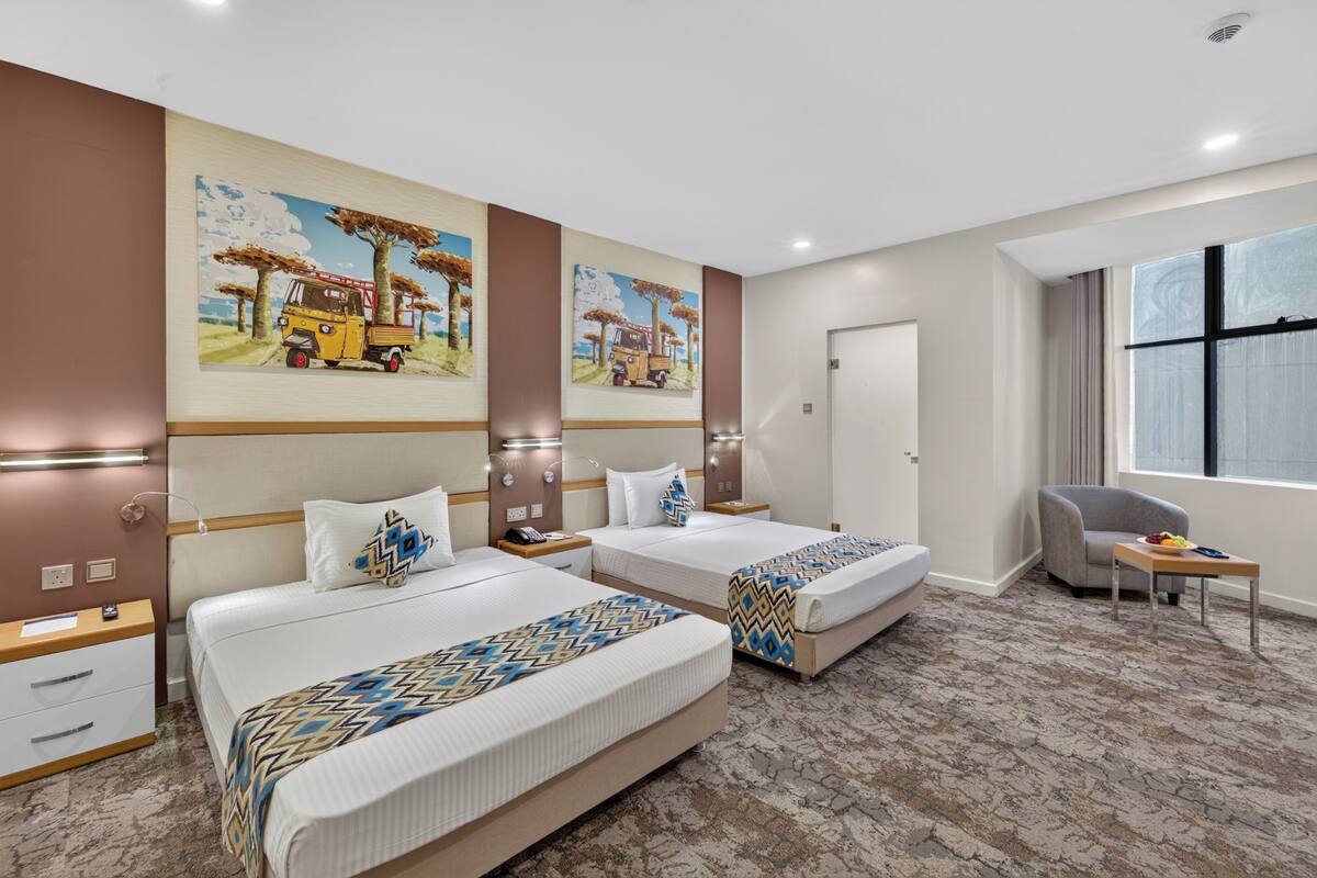 A hotel room with two beds, a chair, a small table, and artwork on the walls.