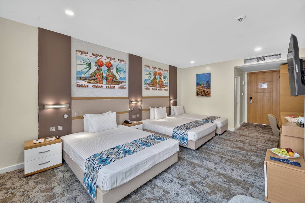 A hotel room with two beds, a desk, a chair, and artwork on the walls.