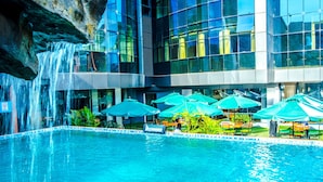A modern hotel with a large indoor pool, waterfall feature, and outdoor seating area with umbrellas.