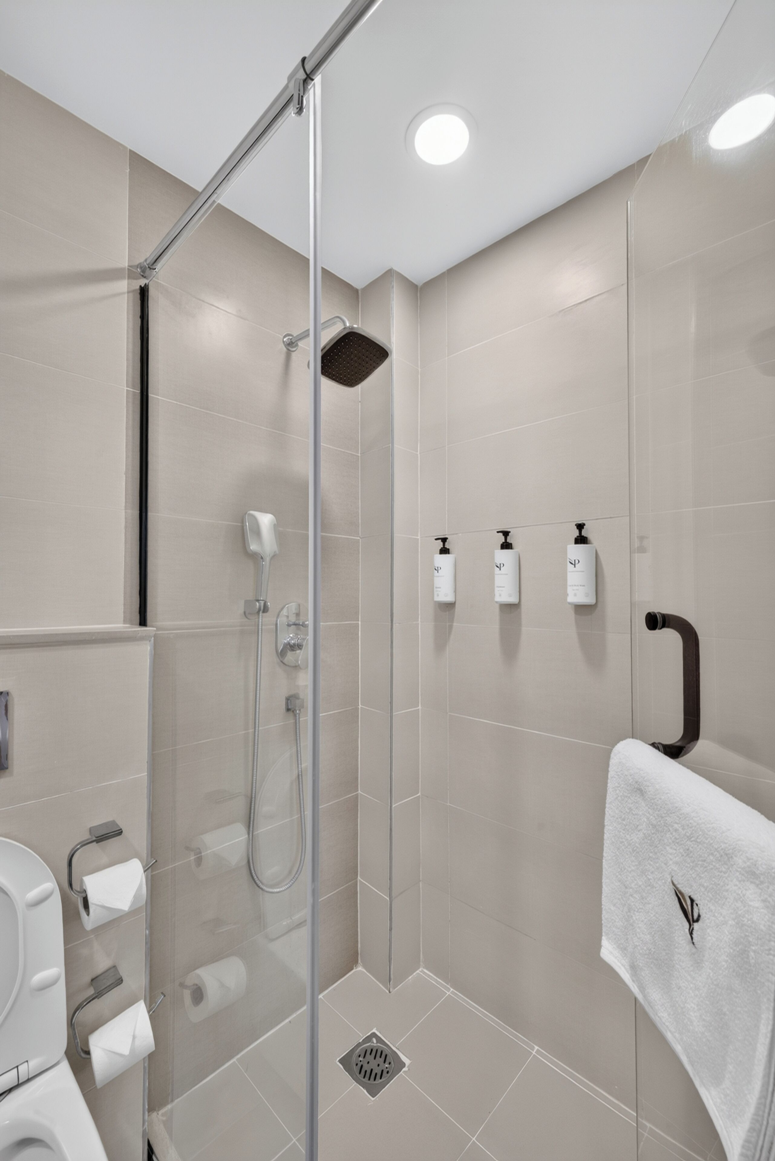 A modern bathroom with a glass-enclosed shower, a toilet with paper towels, and a towel rack with a towel.