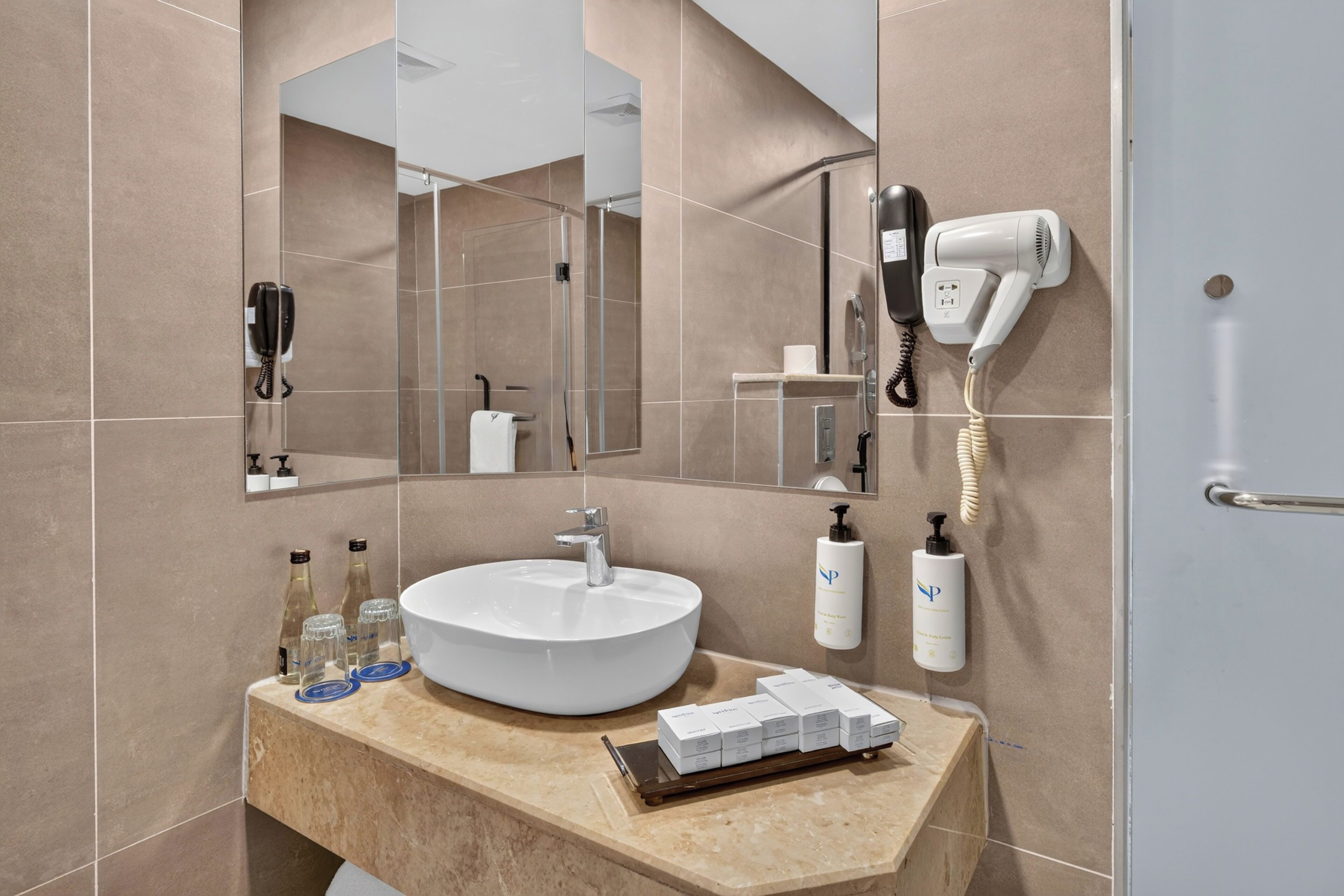 Ein modernes Badezimmer mit einem großen Spiegel, einem weißen Waschbecken und einem an der Wand befestigten Föhn.